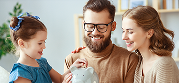 family smiling and putting money into piggy bank